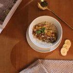 Warm oatmeal with granola and banana slices on a wooden table for a perfect breakfast.